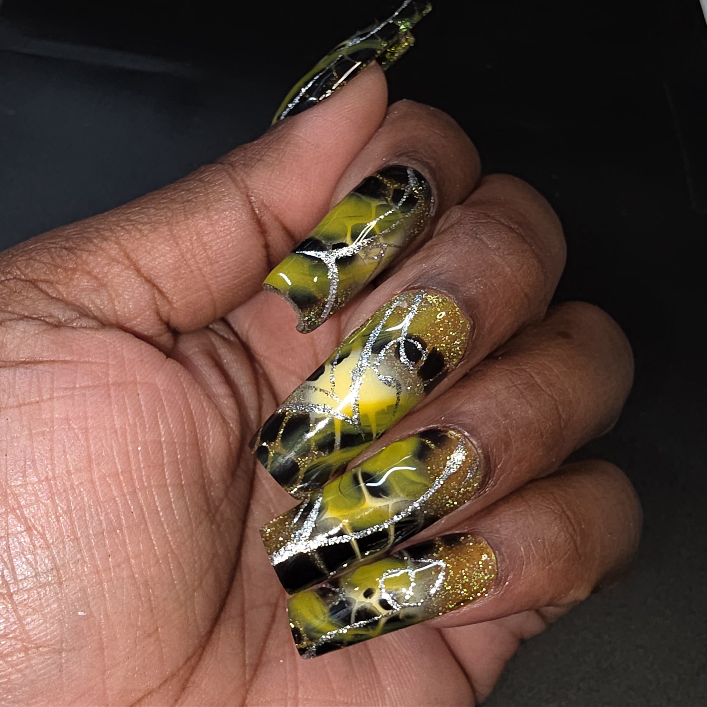 Hand with black and yellow nail art on a dark background