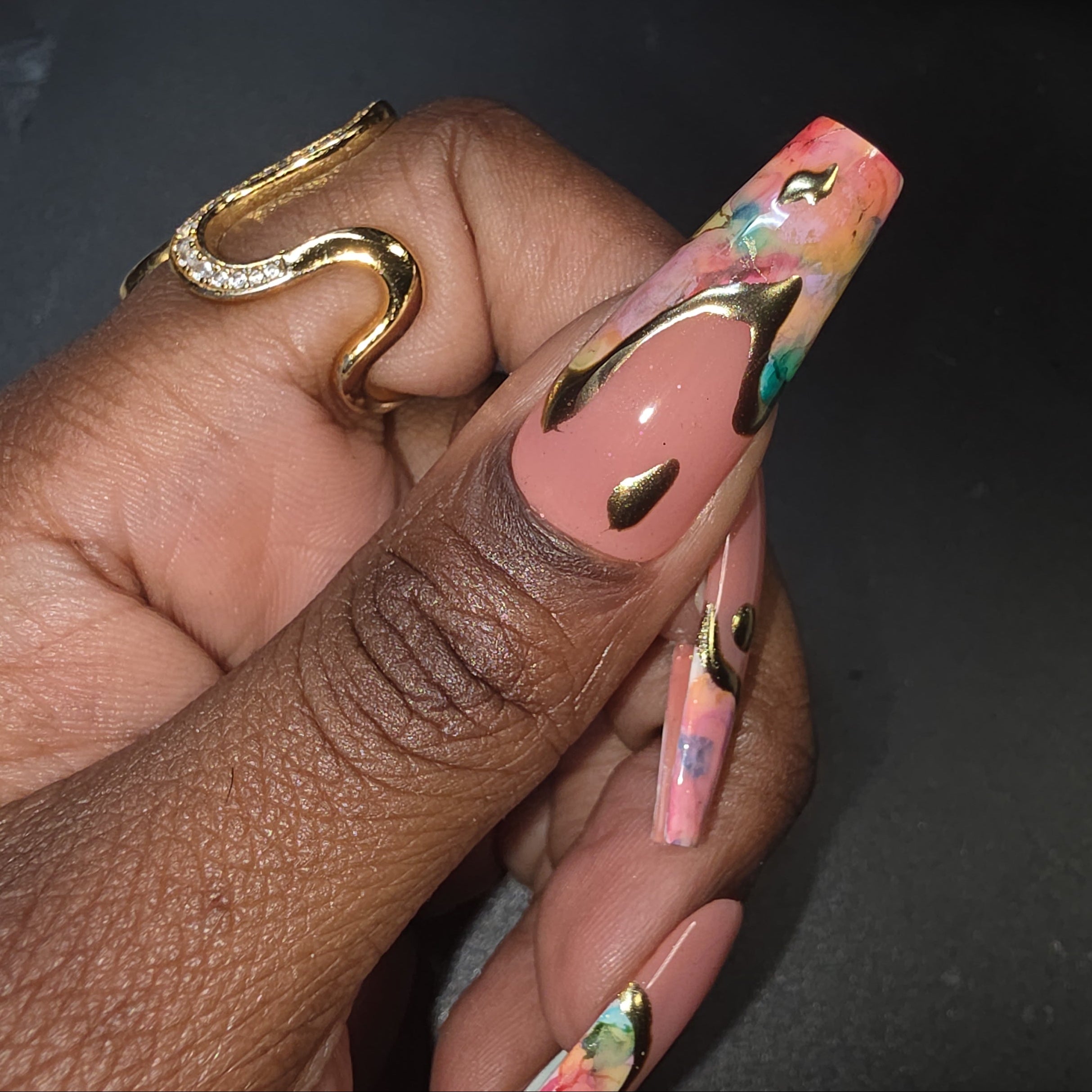 Hand with colorful nail art and gold ring on a dark background
