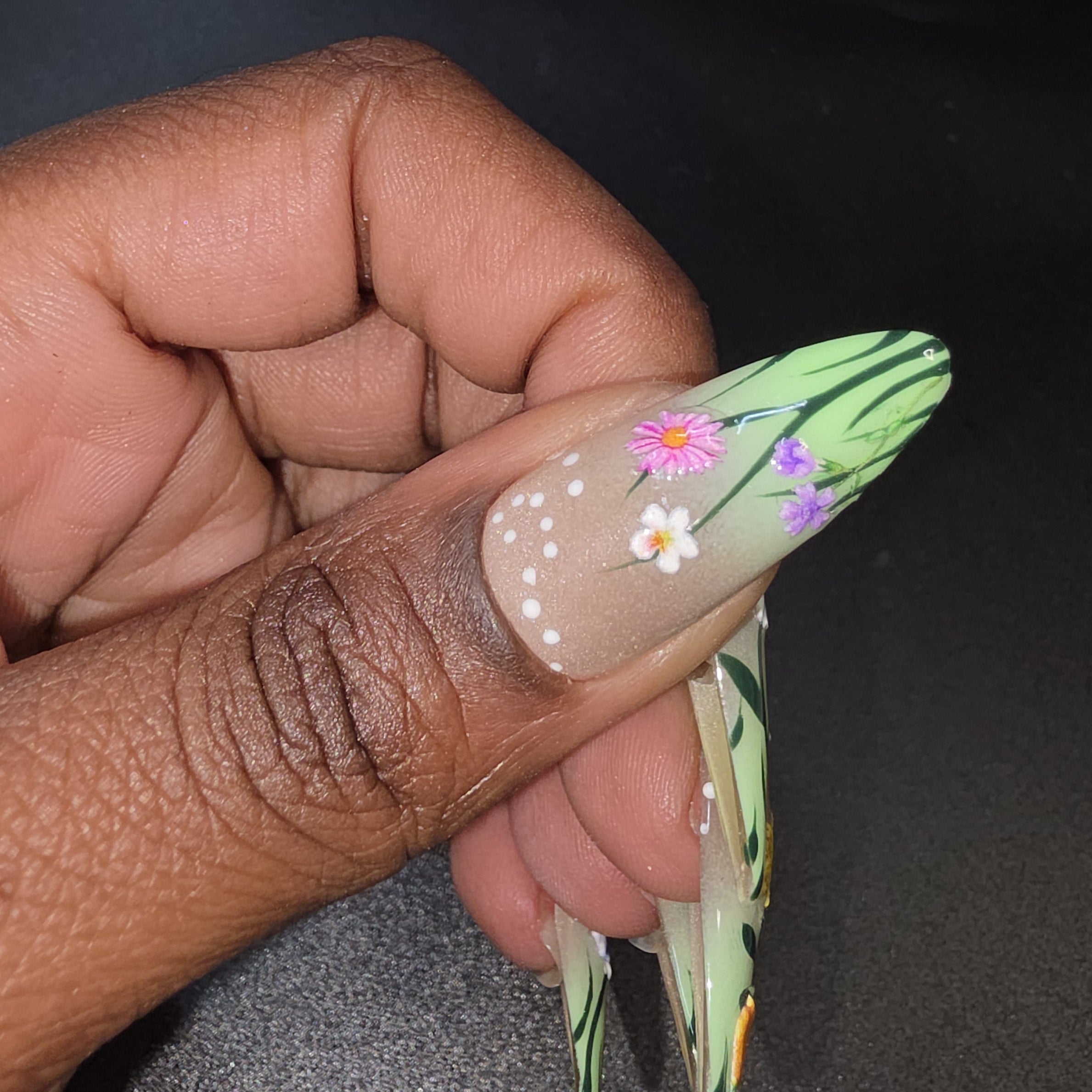 Hand with a long, decorated false nail holding a nail clipper against a dark background