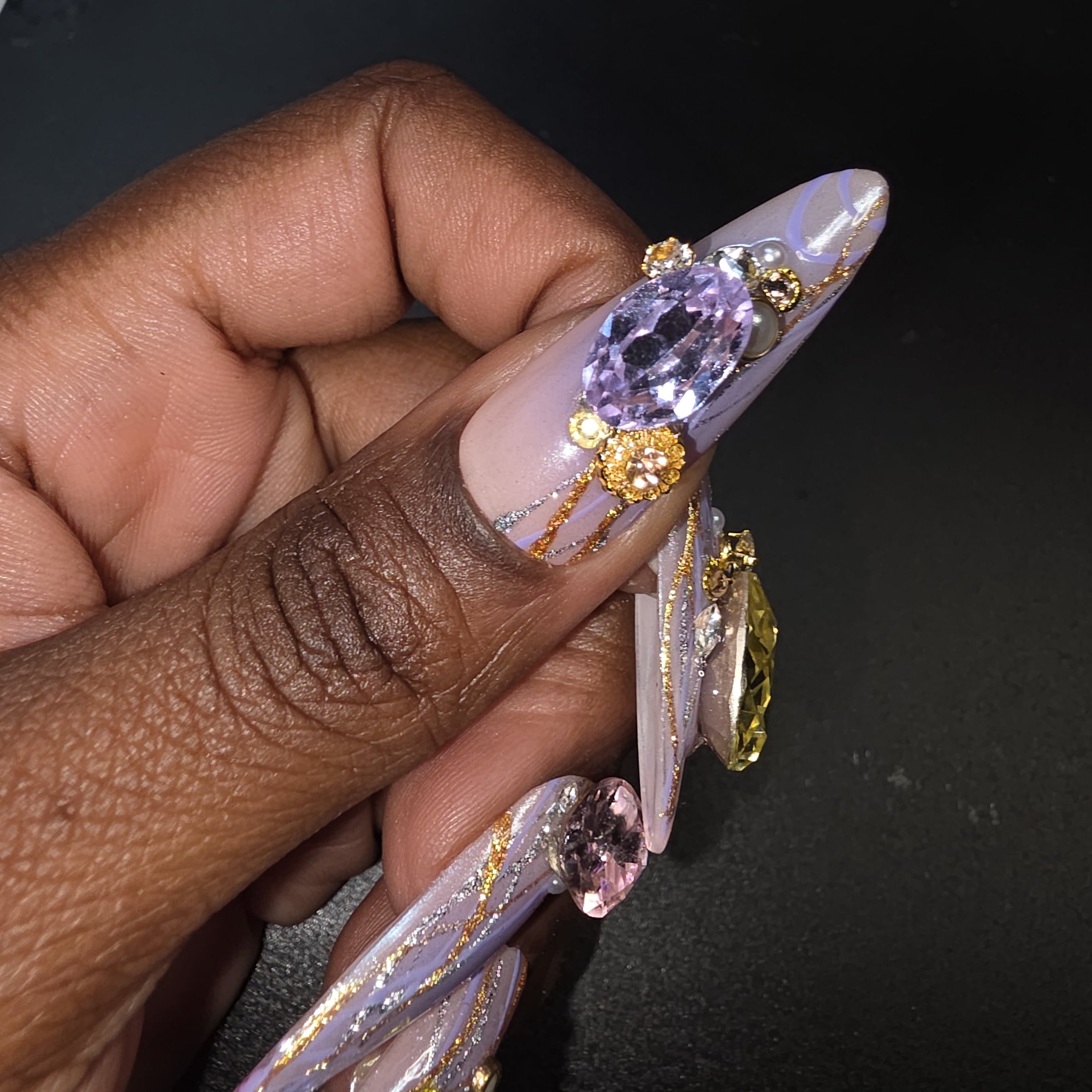 Hand with intricately designed nails featuring gemstones and gold accents against a dark background