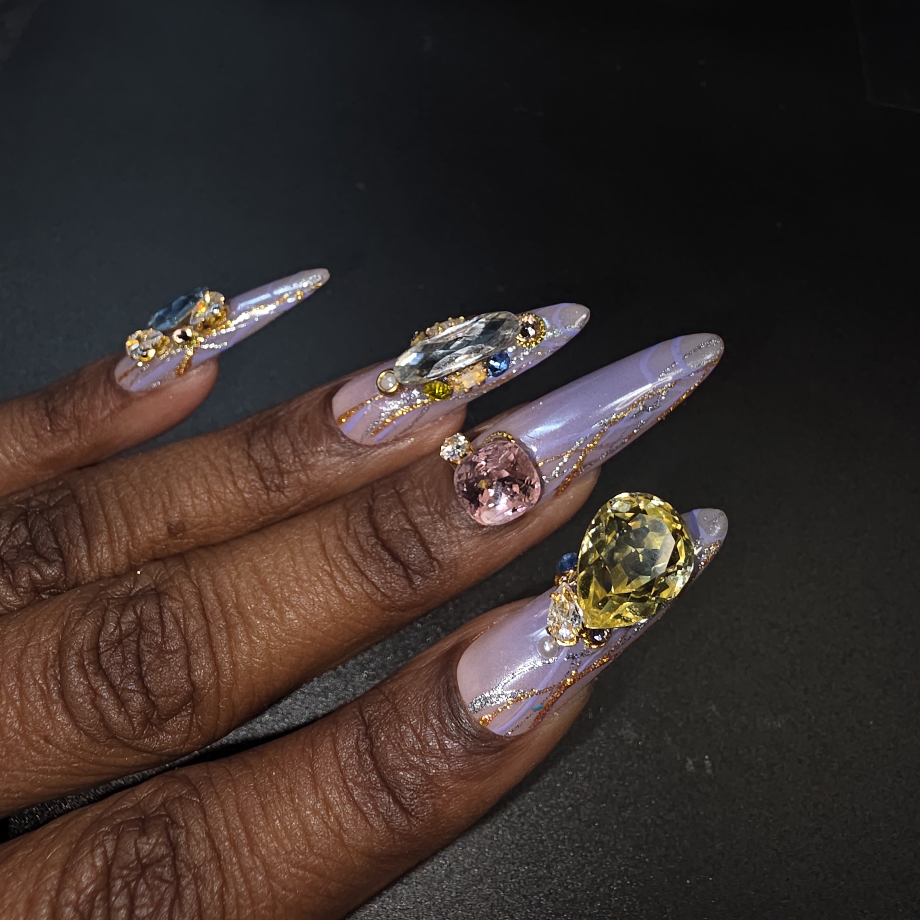 Hand with long, ornately decorated nails featuring gemstones against a dark background