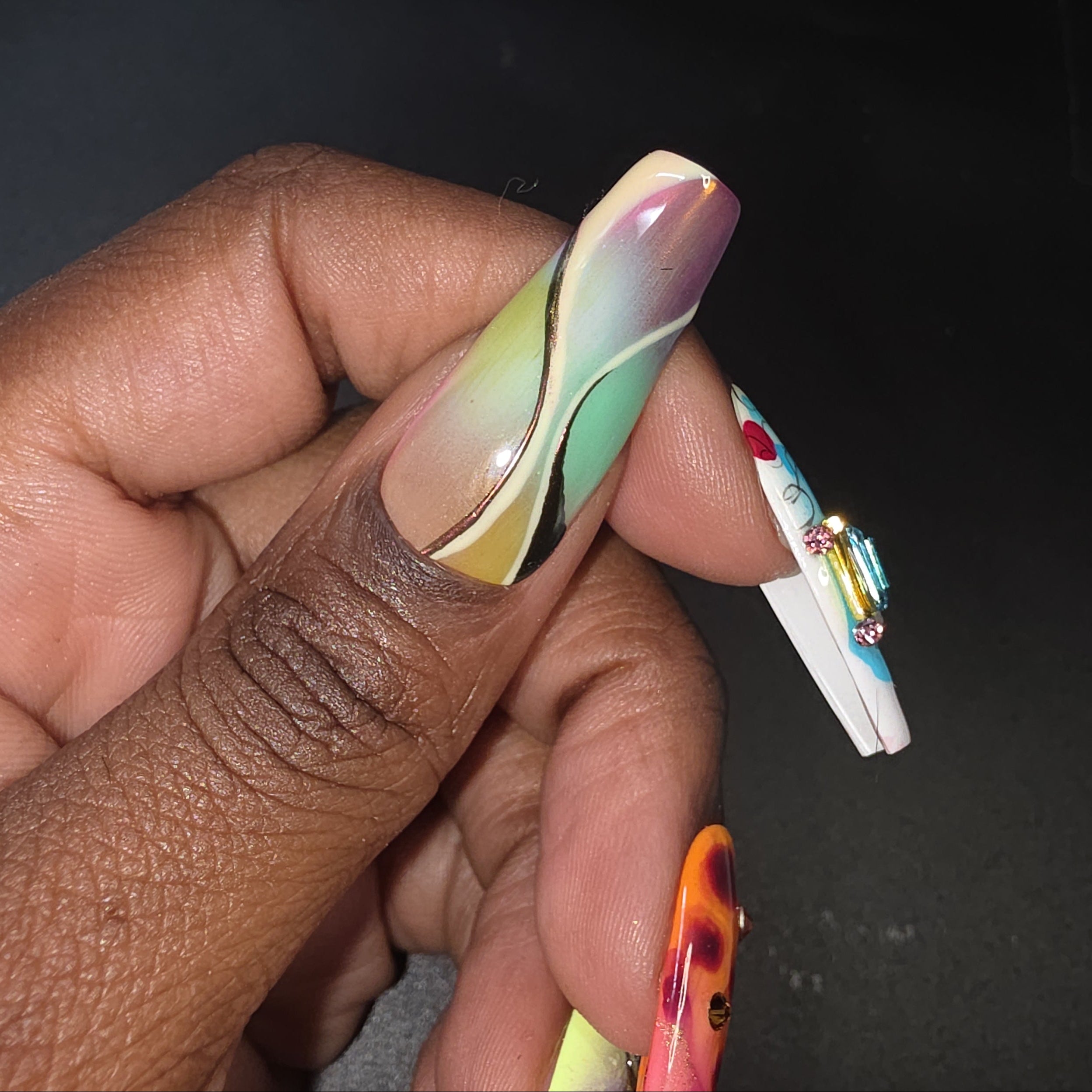 Hand with multicolored nail design holding a small object against a dark background