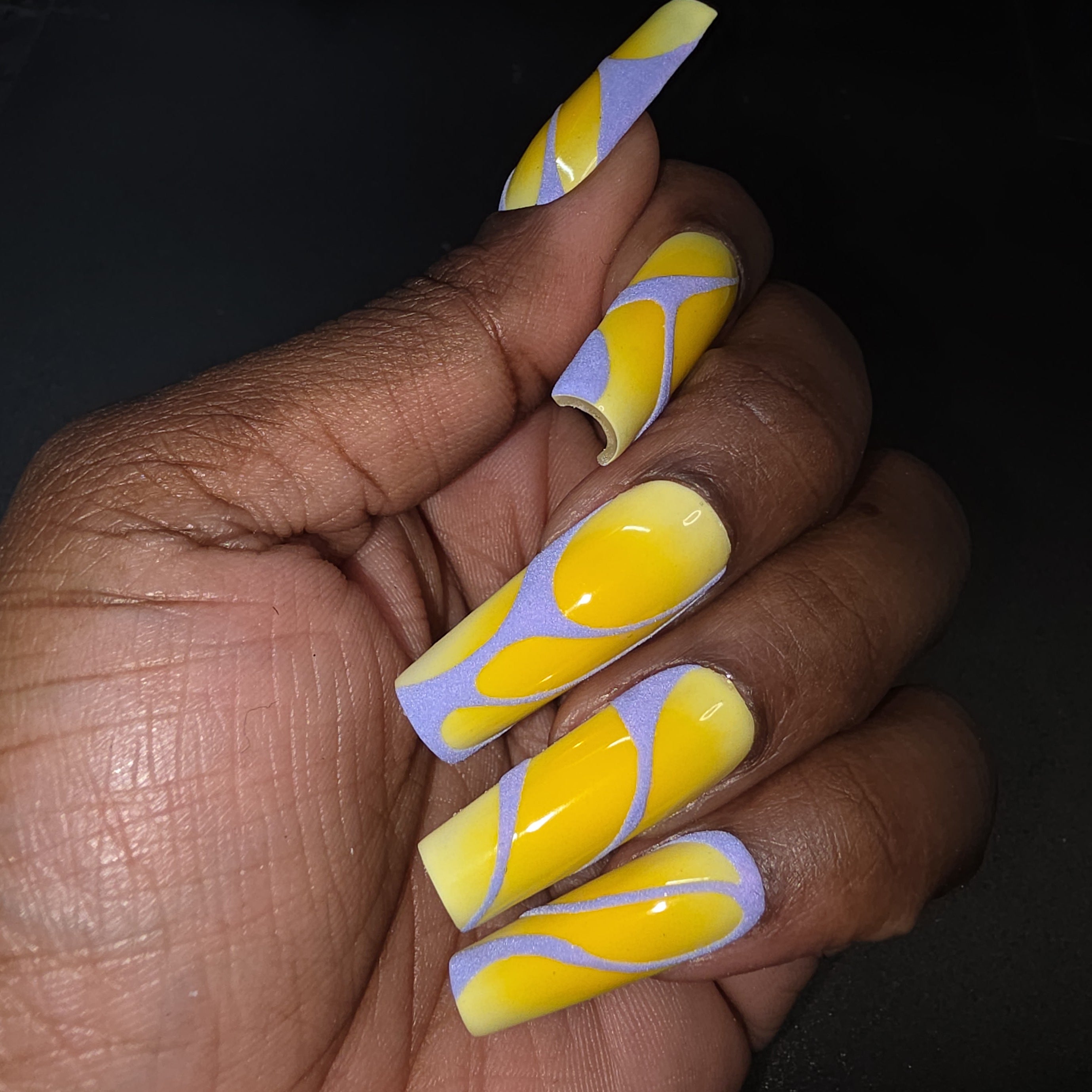 Hand with yellow and purple swirled nail art on a dark background