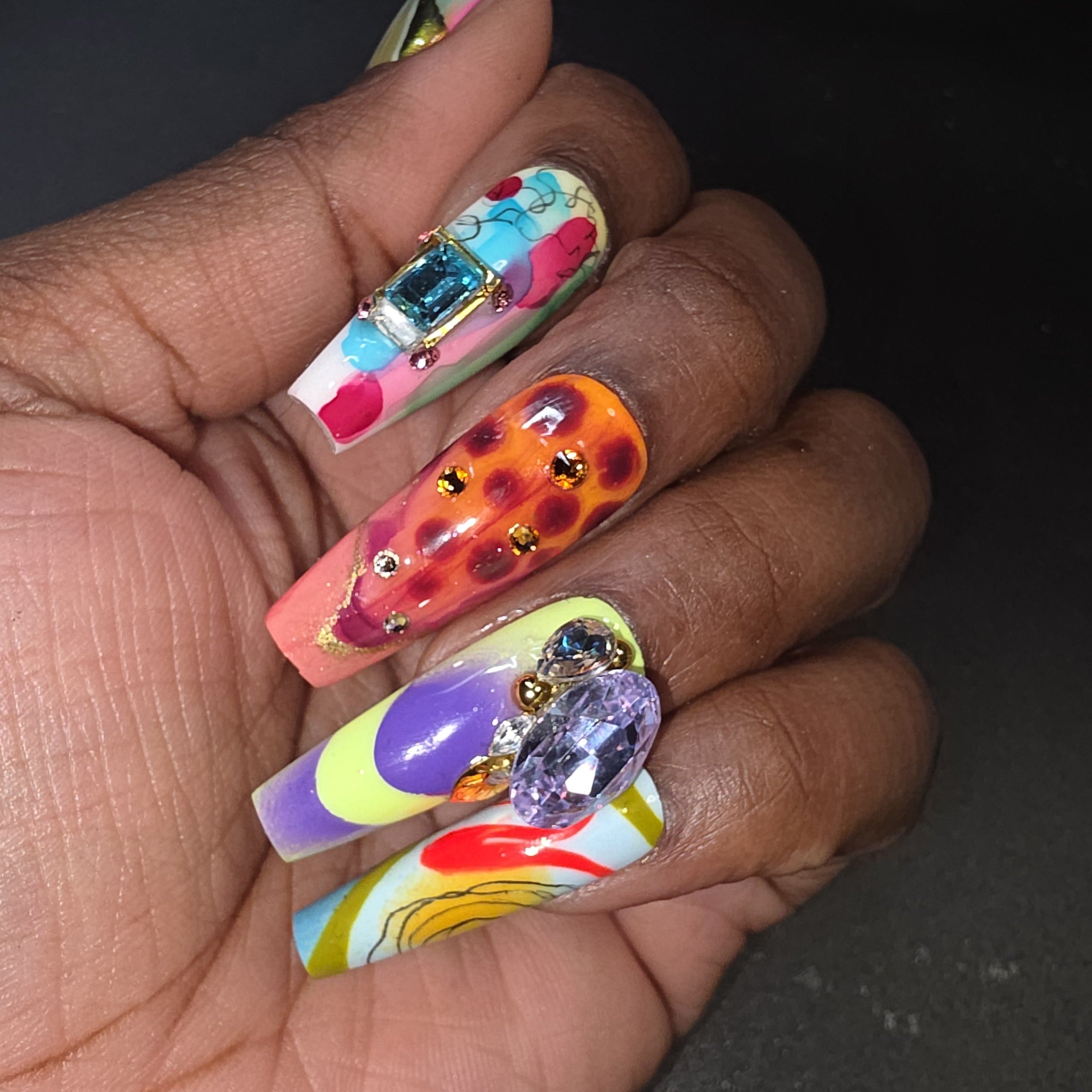 Hand with colorful and intricately designed nails featuring gemstones.