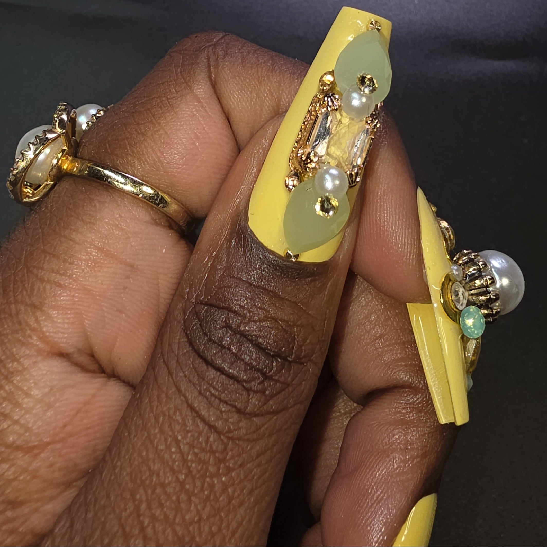 Hand wearing gold and yellow nail art with decorative elements on a dark background